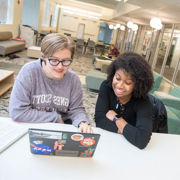 Two students sit by a laptop